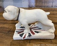Side view of white English bulldog figurine on Union Jack base placed on wooden surface.