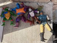 Four assorted vintage action figures including a Teenage Mutant Ninja Turtle and other characters, displayed on a concrete surface.