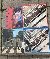 Lot of four vinyl records including three Beatles albums and one Paul McCartney album arranged on pavement.