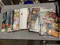 Lot of approximately 17 comic books stacked in plastic sleeves on table, various titles visible including Thor and LEGO comics