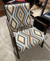 Front and side view of Mid-Century Modern style chair showing geometric patterned cushions in mustard, white, grey, and brown, with wooden frame and armrests.