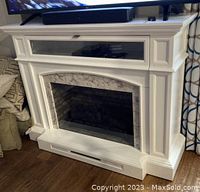 Front view of white electric fireplace with detailed mantel and marble-like interior trim.