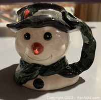 Front view of the Royal Doulton snowman character jug showing the facial features, black hat with holly, and green scarf handle.