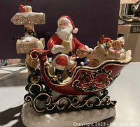 Front view of the figurine on snowy base, showing Santa holding a scroll and two children in sleigh with ornate runners.