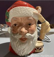 Front and side view of the Royal Doulton Santa Claus Toby Jug showing detailed facial features and doll handle hugging Santa's head.