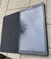 Samsung Galaxy Tab E tablet with black protective cover laid open showing front screen and physical buttons below the screen.