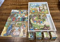 Photo of the four assembled block puzzles and matching picture guides spread on a wooden surface, showing scenes from Snow White and the Seven Dwarfs