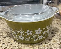 Side view of the Pyrex 473 casserole dish showing the olive green exterior with white Spring Blossom flower pattern and clear glass lid on top.