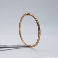 Side view of the 14K yellow gold bangle bracelet showing its circular mesh design.