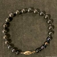 Full view of the black pearl bracelet showing the string of black pearls and the gold clasp.