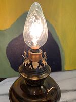 Close-up of Kosmos Brenner electric lamp showing flame-shaped bulb and ornate metal crown holder with original tag