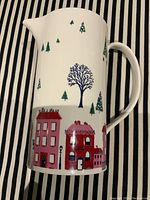 Side view showing town buildings and pine trees design on the jug with handle and spout