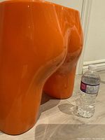 Photo of one section of the orange acrylic display/planter next to a water bottle for scale, showing its glossy surface and curved shape.