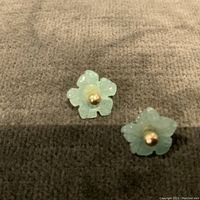 Close-up photo of a pair of small flower-shaped earrings carved from light green jade, with a 14K yellow gold dome center