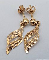 Pair of 14K yellow gold drop earrings laying flat showing front design with textured open leaf shape and ball stud.