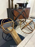 Three decorative metal orbs arranged on a table with wooden and circular bases visible. Background shows cabinet and decorative vases.