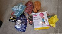 Overview of the lot showing baseball gloves, baseball practice balls, golf balls, hockey pucks, bike bells, and tire repair materials along with a boxed stability ball.