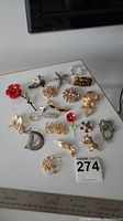 Full view of all brooches laid out on a white surface showing approximately 18 different brooches in various shapes and colors.