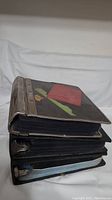 Three thick binders stacked showing wear and decoration on binder covers