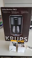 Front image of the sealed Krups FME2 coffee maker box showing product image and features.