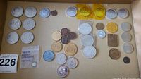 Wide photo of the full coin collection on cardboard showing different coin types including gold and silver toned coins, and a few uniquely shaped coins.