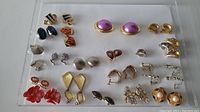 Full display of thirty pairs of vintage earrings in various styles and colors on acrylic holder.