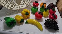 Full set of colorful Murano glass fruits and vegetables arranged with metal basket in background.