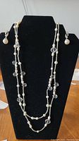 Full view of the double-strand pearl necklace with clear beads on a black display stand.