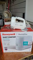 Black & Decker PowerPro hand mixer with two metal beaters and Honeywell Quiet Comfort humidifier in box on wooden surface.