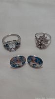 Two rings with clear stones and two blue enamel sterling silver clip-on earrings with castle design