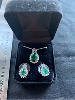 Necklace pendant and earrings displayed in black box showing pear-shaped green stones surrounded by clear stones
