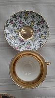 Photo of a floral pattern saucer with pink and yellow flowers and a matching porcelain tea cup with gold band