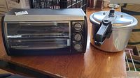 Photo showing toaster oven and pressure cooker side by side on wooden table.