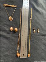Top-down photo of three cameo necklace and earring sets along with a cameo tie clip and ruler for size reference