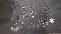Overview of laid-out assorted vintage jewelry including necklaces, rings, earrings, and brooches on dark floor.