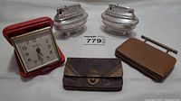 Overview of all lot items: two silver-tone Ronson Queen Anne lighters, two vintage change purses, and red Seth Thomas portable alarm clock.