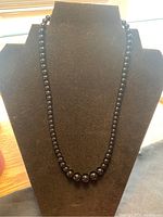 Polished black onyx bead necklace displayed on stand showing graduated beads