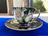 Side view of Aynsley teacup and saucer displaying floral pattern and gold trim on dark background.