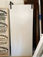 Front view of white barn door standing vertically with black metal sliding hardware mounted on top.