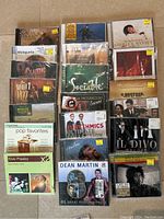 Photo of 19 CDs featuring multiple artists including Elvis Presley, Bob Marley, Dean Martin, Il Divo, and others in jewel cases, mostly new or with price tags