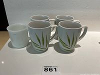 Five mugs displayed: four Corelle mugs with green leaf pattern and one worn white Anchor Hocking mug.