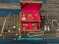 Full lot layout showing multiple gold tone necklaces, earrings, rings, brooches spread out beside an open wooden jewelry box with pink lining.