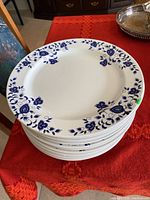 Stack of 12 white ceramic plates with blue floral rim design on a red tablecloth.