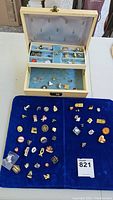 Overview photo showing pins organized on two blue velvet pads alongside an open wooden jewelry box containing pins inside lined compartments.