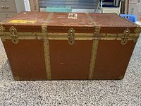 Front view showing the full length of the brown leather steamer trunk with brass trim, locking clasps and rivets.
