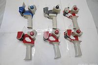 Six handheld packaging tape rollers arranged on a white surface showing the variety of colors and metal frames.