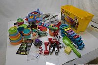 Overview photo of the entire collection including LEGO Classic yellow container, blue airplane, xylophone, stacking cups, toy vehicles, and assorted toys spread on a white surface.