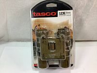 Front view of new sealed Tasco 12x25 Essentials binocular in plastic packaging with camouflaged rubber armor.