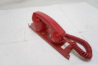 Side angled view of the red Siemens analog phone on metal mounting base, handset on cradle, showing coiled cord.