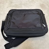 Front view of black Dell laptop bag showing fabric and Dell logo on front corner, with attached shoulder strap.